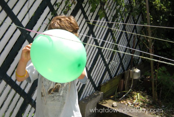 Boy holding green balloon attached to string in backyard for a balloon rocket experiment.