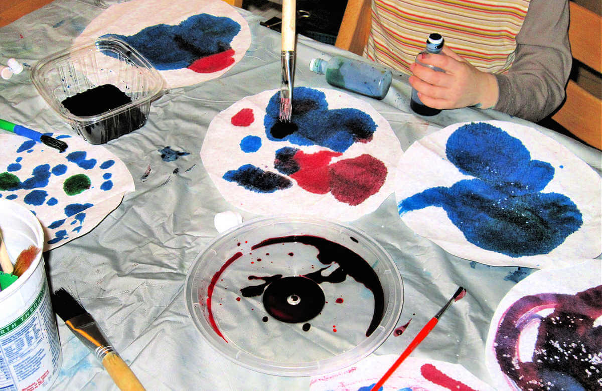 Child applying blue, red and green paint to coffee filter art projects