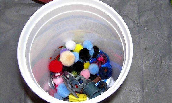 Container filled with pompoms and small items for shaken container art project.