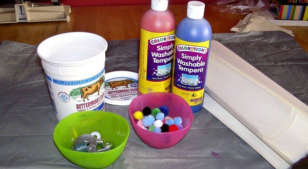 Supplies for shaken container painting including paint bottles, empty plastic container, paint and small items in two plastic bowls.