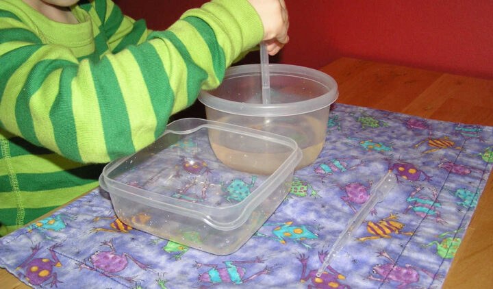 Child using pipette for water transfer activity.