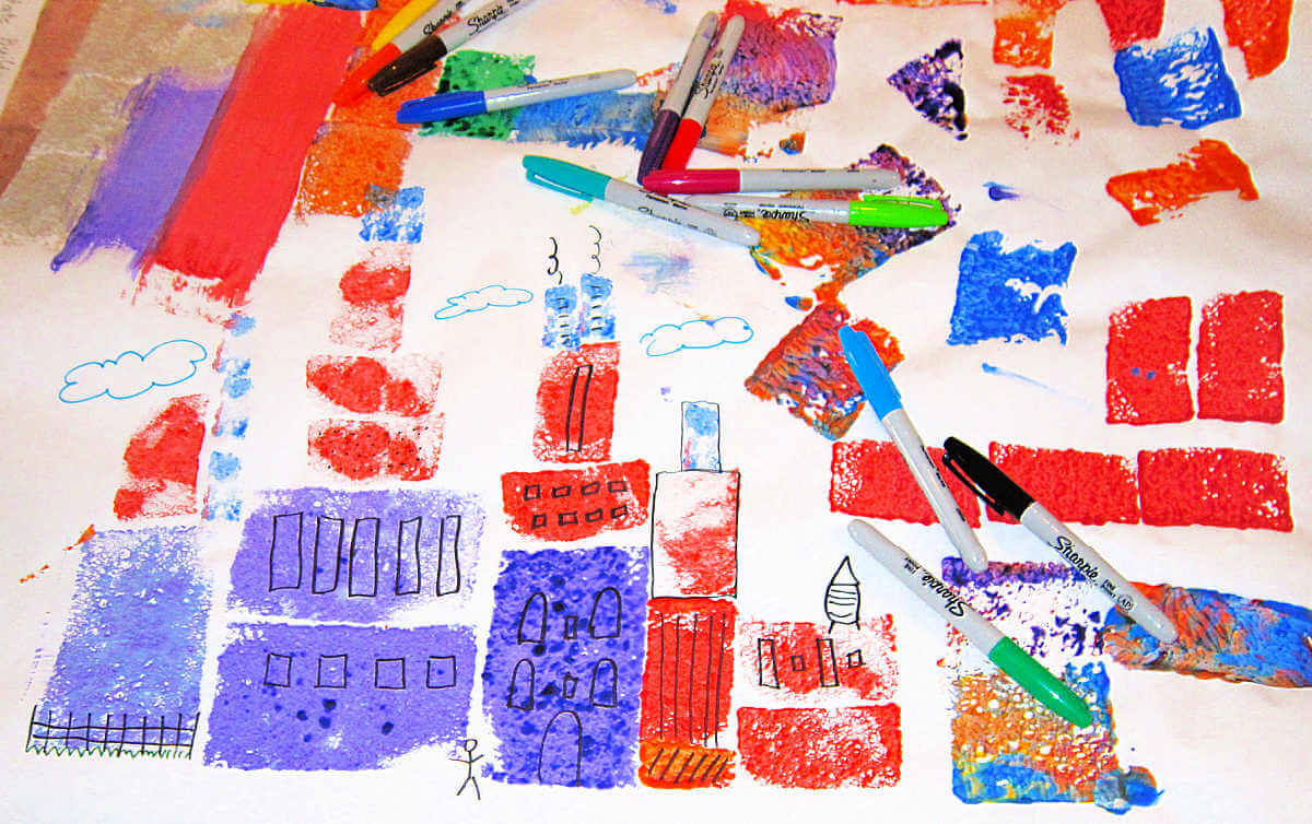 Children's art project of a skyline created by sponge painting shapes with markers scattered on top.