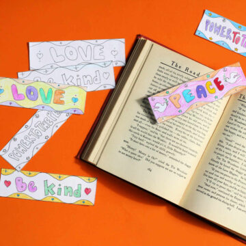 Paper bookmarks with kindness and peace messages next to and on top of open book.