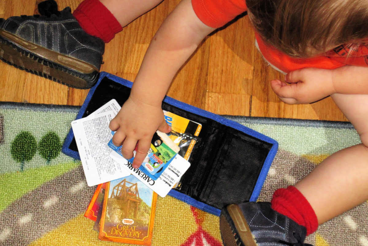 toddler playing with cards in toy wallet on floor