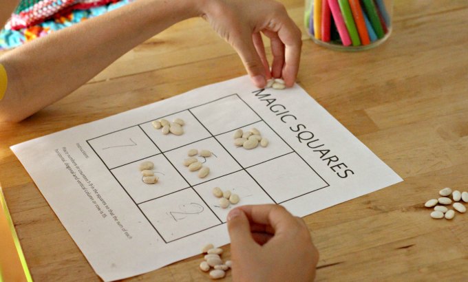 Playing a 3x3  magic square math puzzle with printable. Hands placing beans on different squares. 