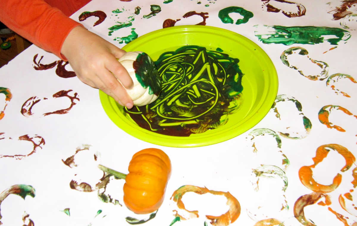 Dipping mini pumpkins into paint and stamping on paper