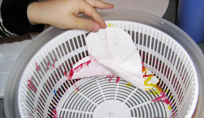 Child removing heart shaped painted paper from salad spinner