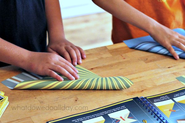 Two children side by side folding paper airplanes.