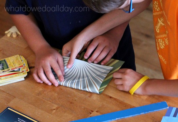 Two children working together to fold paper airplane.