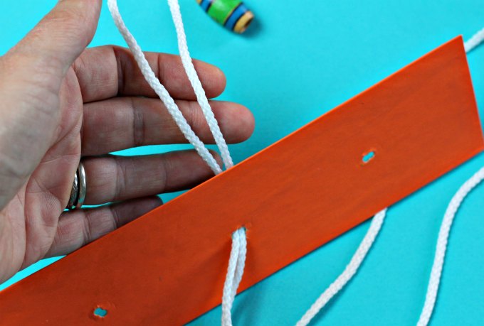 Hand pulling string through center hole in narrow orange board.